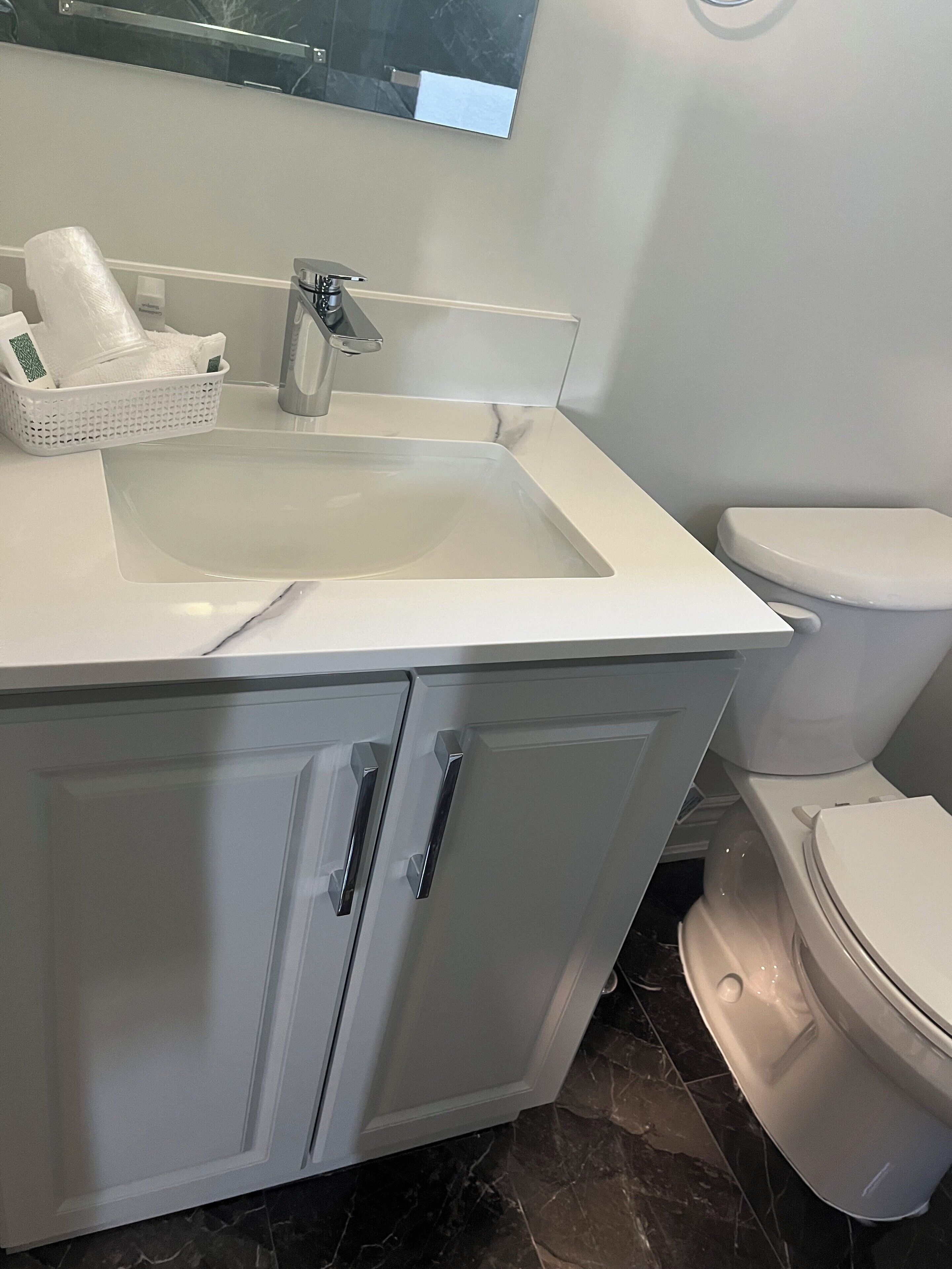 A bathroom with a white sink, a mirror, a toilet, and a basket of toiletries.