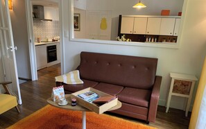 Ein Wohnzimmer mit braunem Sofa, einem kleinen Holztisch mit einer Zeitschrift, einer Tasse und einem Marmeladenglas.