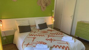 Una cama bien tendida con una manta estampada, una pared verde y un aparador verde.