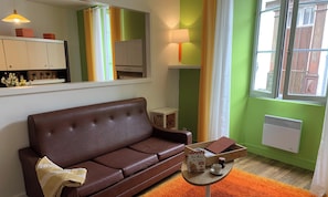 Ein braunes Leder Sofa, ein kleiner runder Tisch mit einer Schachtel und einer Tasse, ein Spiegel, ein Fenster mit Vorhängen und eine Heizung.