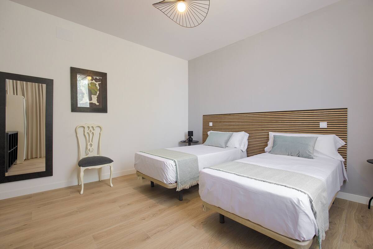 Une chambre avec deux lits, une chaise, un miroir et un luminaire au plafond.