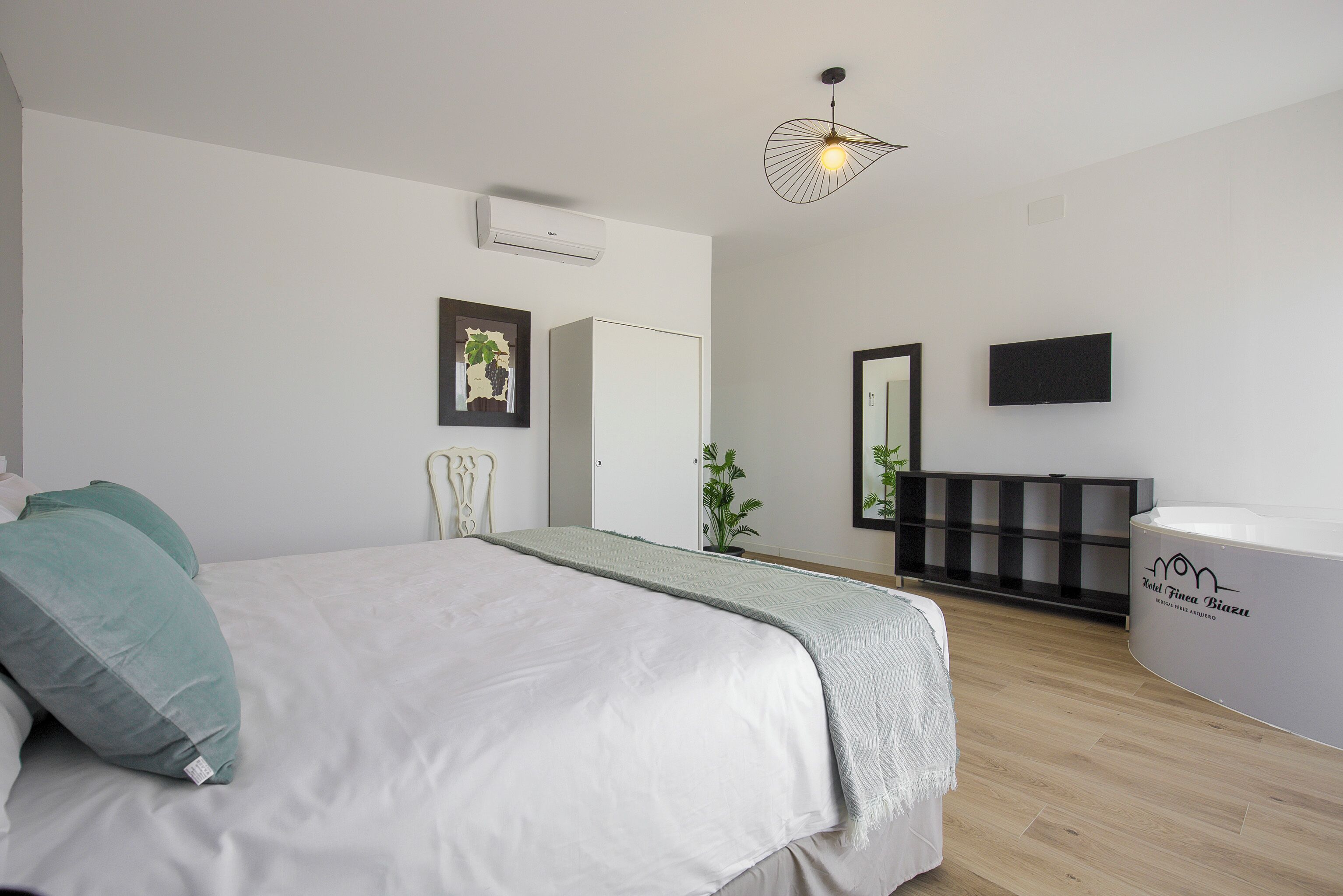 Un dormitorio moderno con cama, mesita de noche, espejo, televisor y bañera integrada.