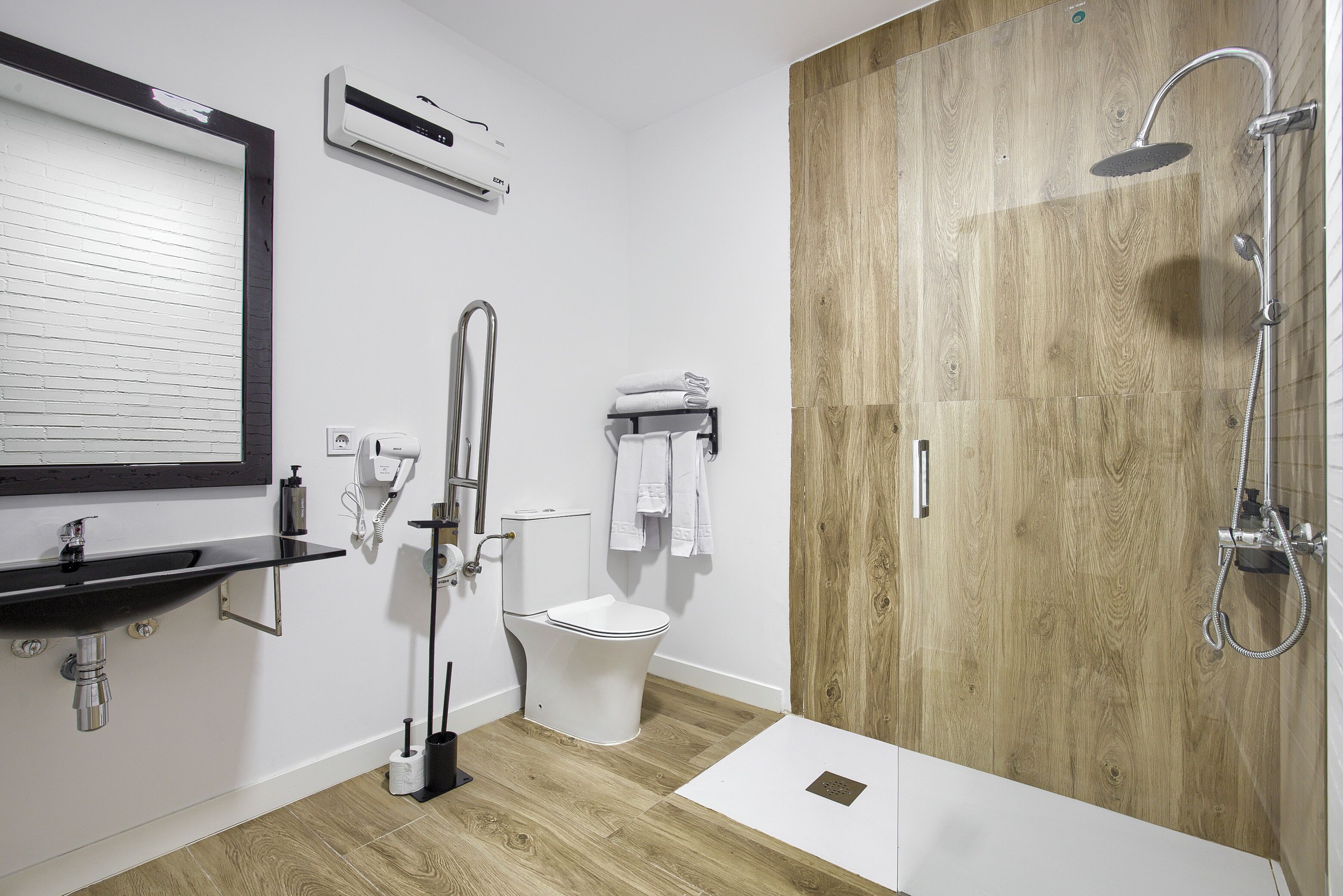 Un baño moderno con tocador de madera, inodoro, ducha y toallero.