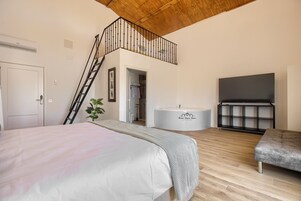 A bedroom with a bed, a bench, a bathtub, and a TV.