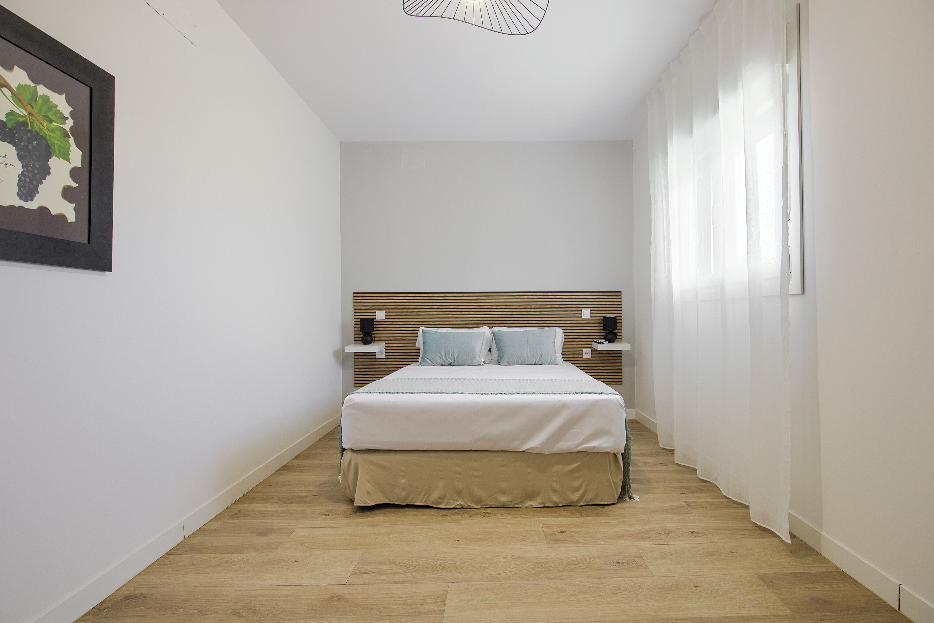 A bedroom with a wooden headboard, a bed with white bedding, two bedside tables, and a framed picture on the wall.