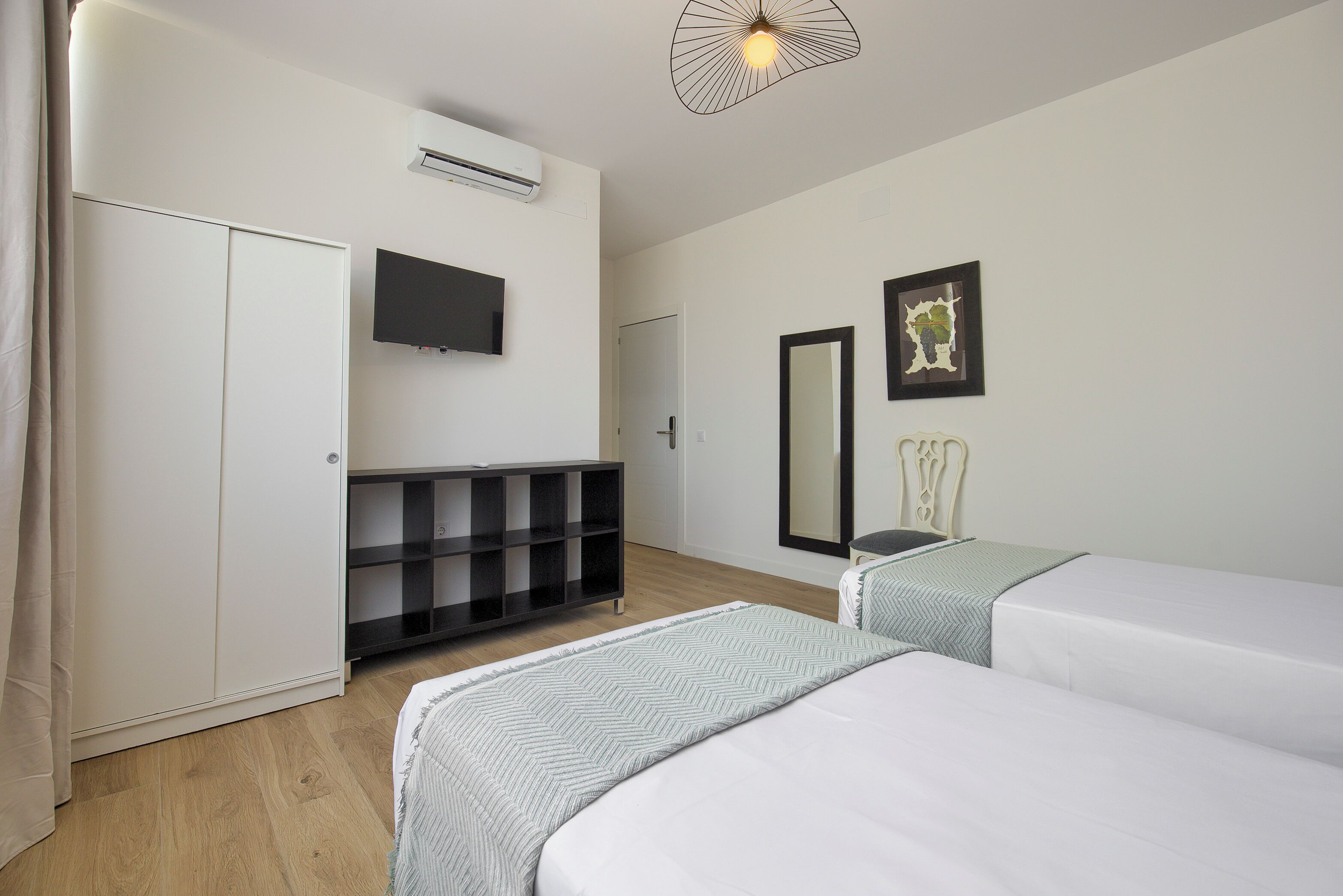 Een hotelkamer met een kledingkast, televisie, bed, nachtkastje, spiegel en een wandlamp.