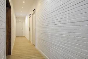 Pasillo con paredes de ladrillo blanco y piso de madera, que conduce a una puerta con el nombre 'Macarena'.