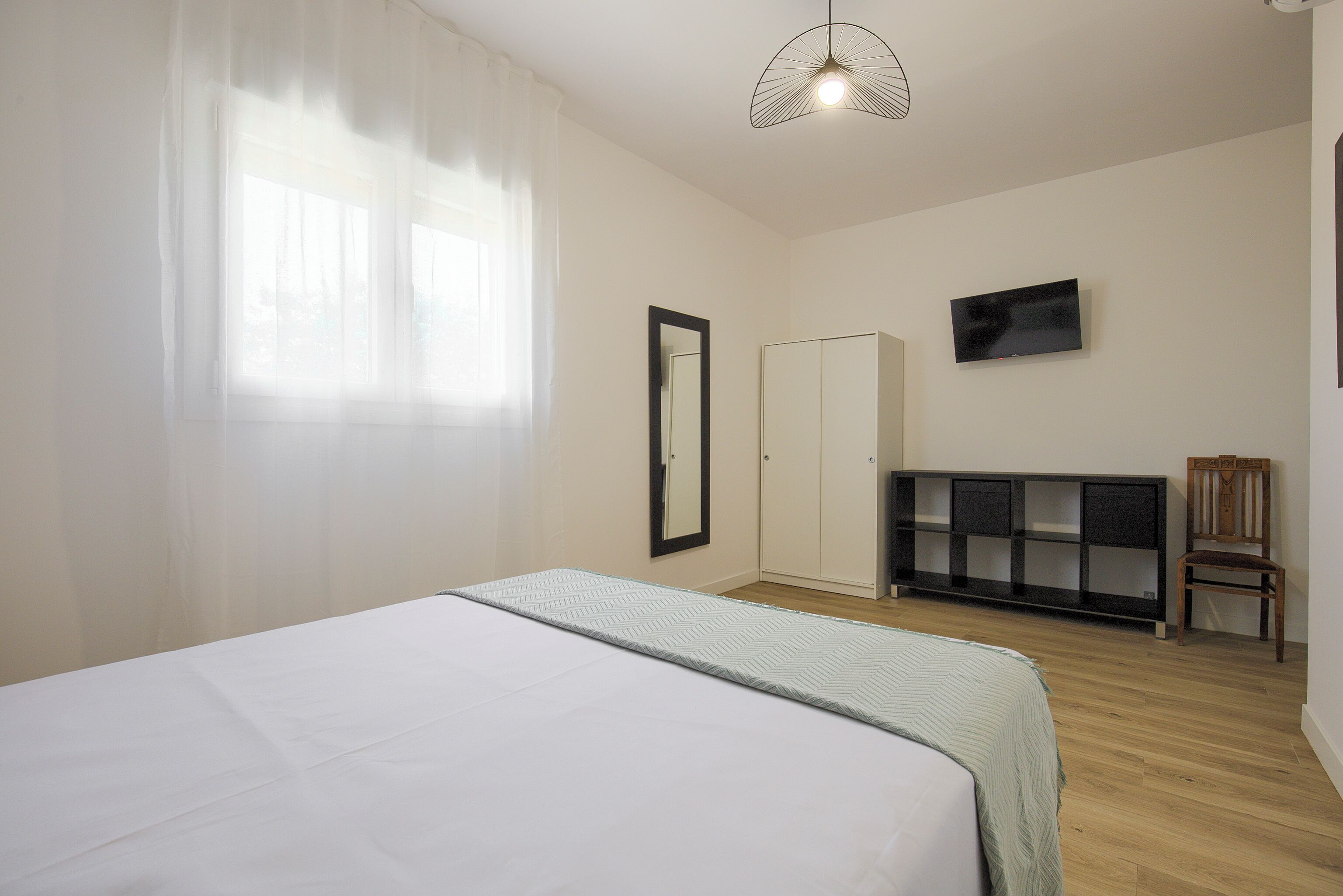 Un dormitorio con cama, armario, televisor y silla.