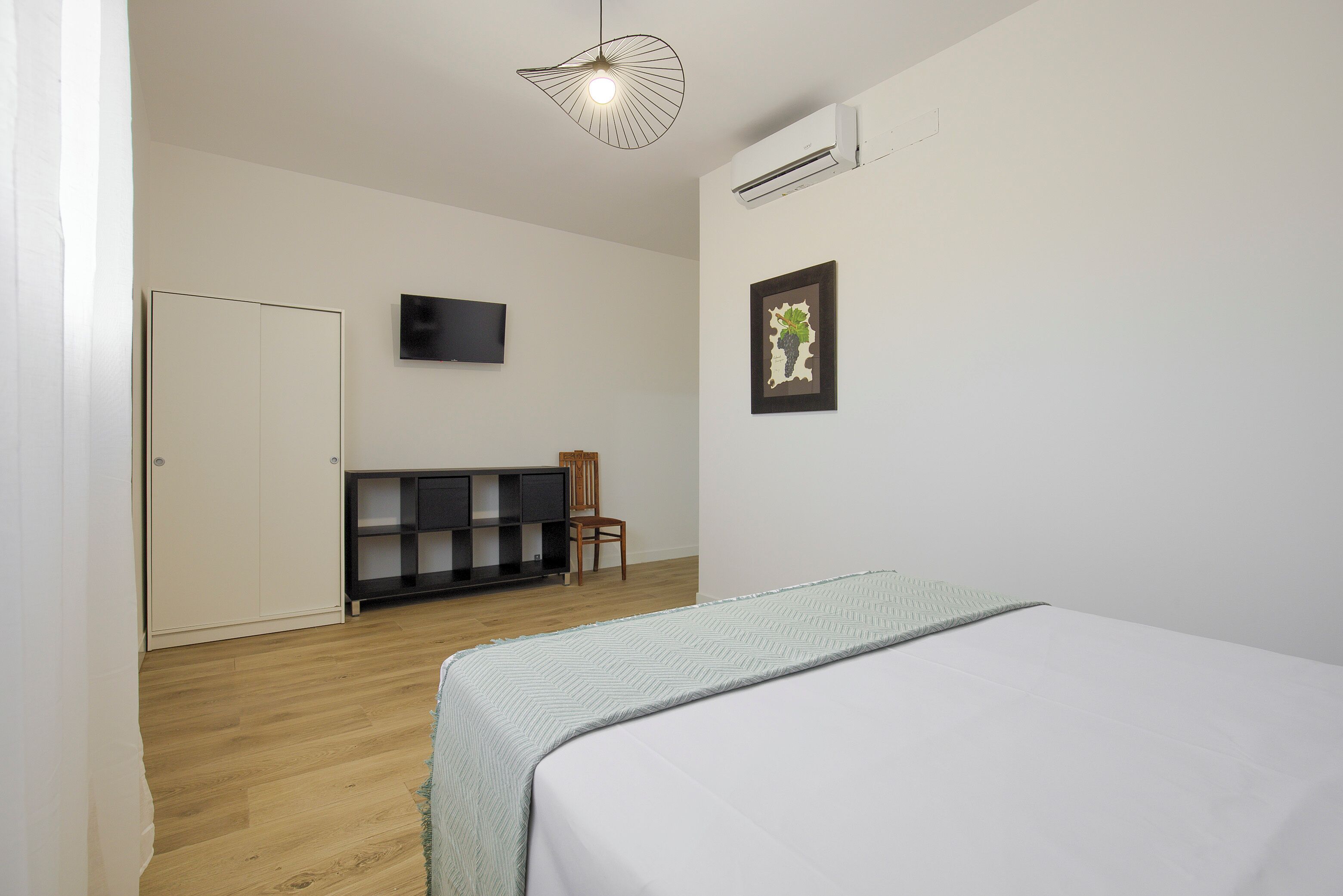 Une chambre à coucher comprenant un lit, une chaise, un téléviseur et un climatiseur fixé au mur.