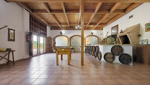 Una habitación amplia con suelo de baldosas, vigas de madera en el techo, una mesa central y un expositor de barriles a la derecha.