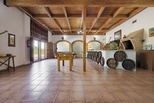 A spacious room with a tiled floor, wooden beams on the ceiling, a central table, and a barrel display on the right.