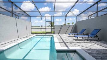 A swimming pool with a glass ceiling, surrounded by lounge chairs and a view of palm trees.