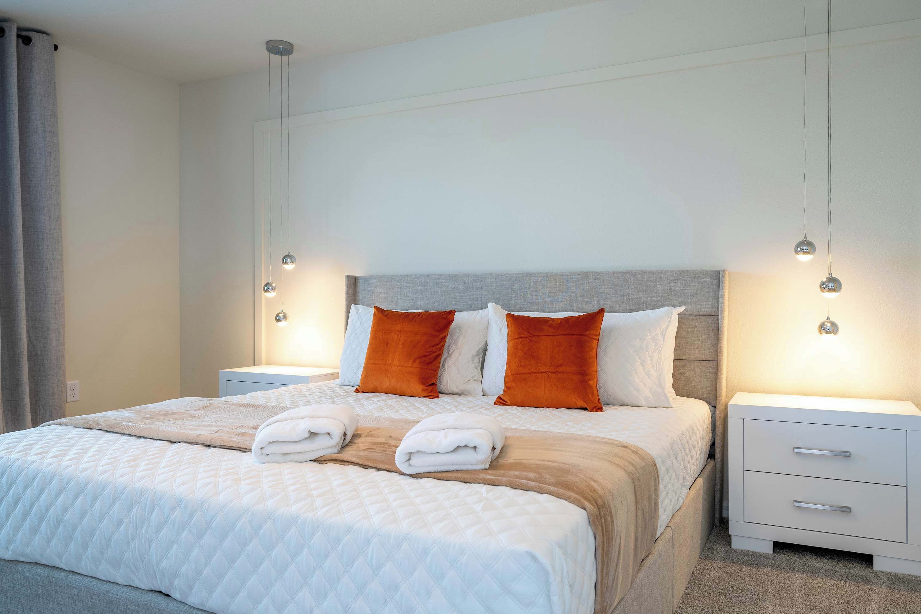 A neatly made bed with white and orange bedding, two bedside tables with lamps, and a grey headboard.