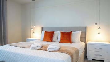 A neatly made bed with white and orange bedding, two bedside tables with lamps, and a grey headboard.