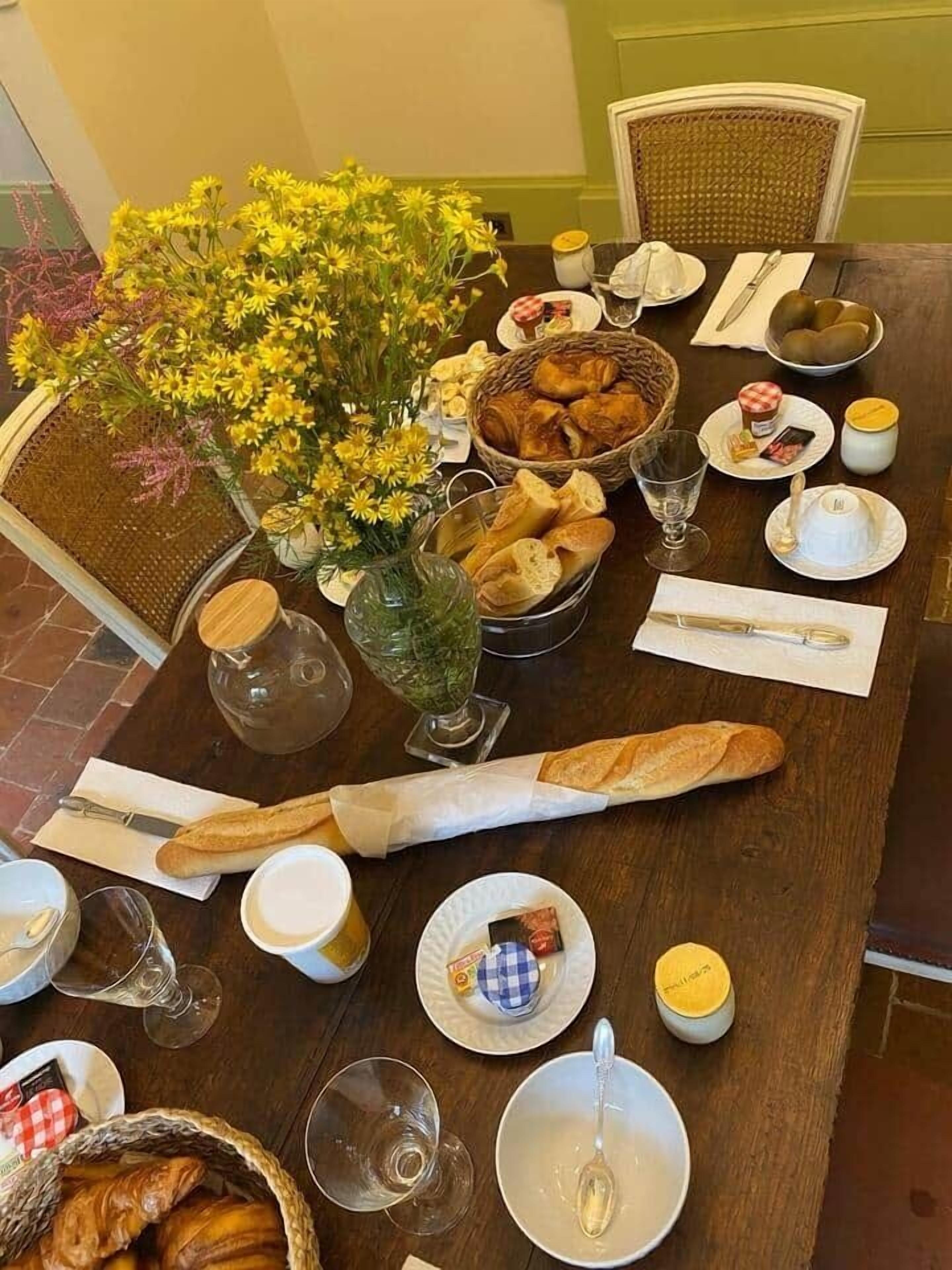 A dining table set with bread, pastries, a vase of yellow flowers, and various condiments.