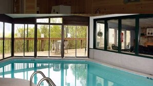 An indoor swimming pool with clear glass walls, a metal ladder, and a wooden deck outside. - Stunning Mountain Views with Community Amenities! (Gatlinburg)