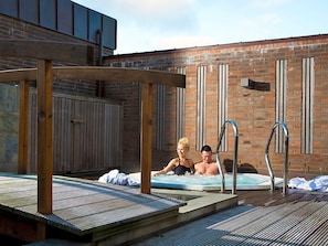 Une terrasse en bois avec un jacuzzi et des échelles en métal.