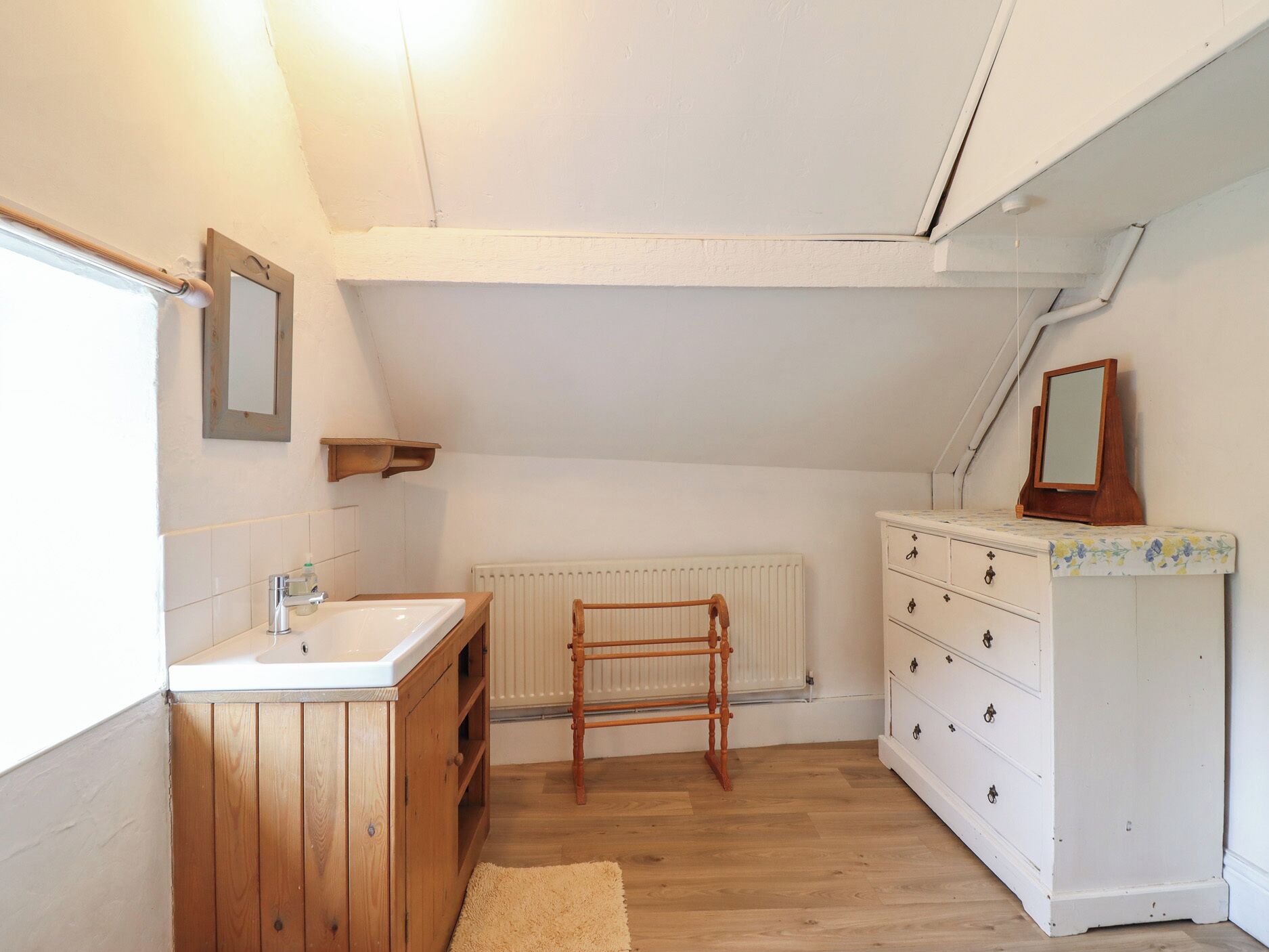 A small, compact bathroom with a wooden cabinet, a white sink, a radiator, and a white dresser with drawers.