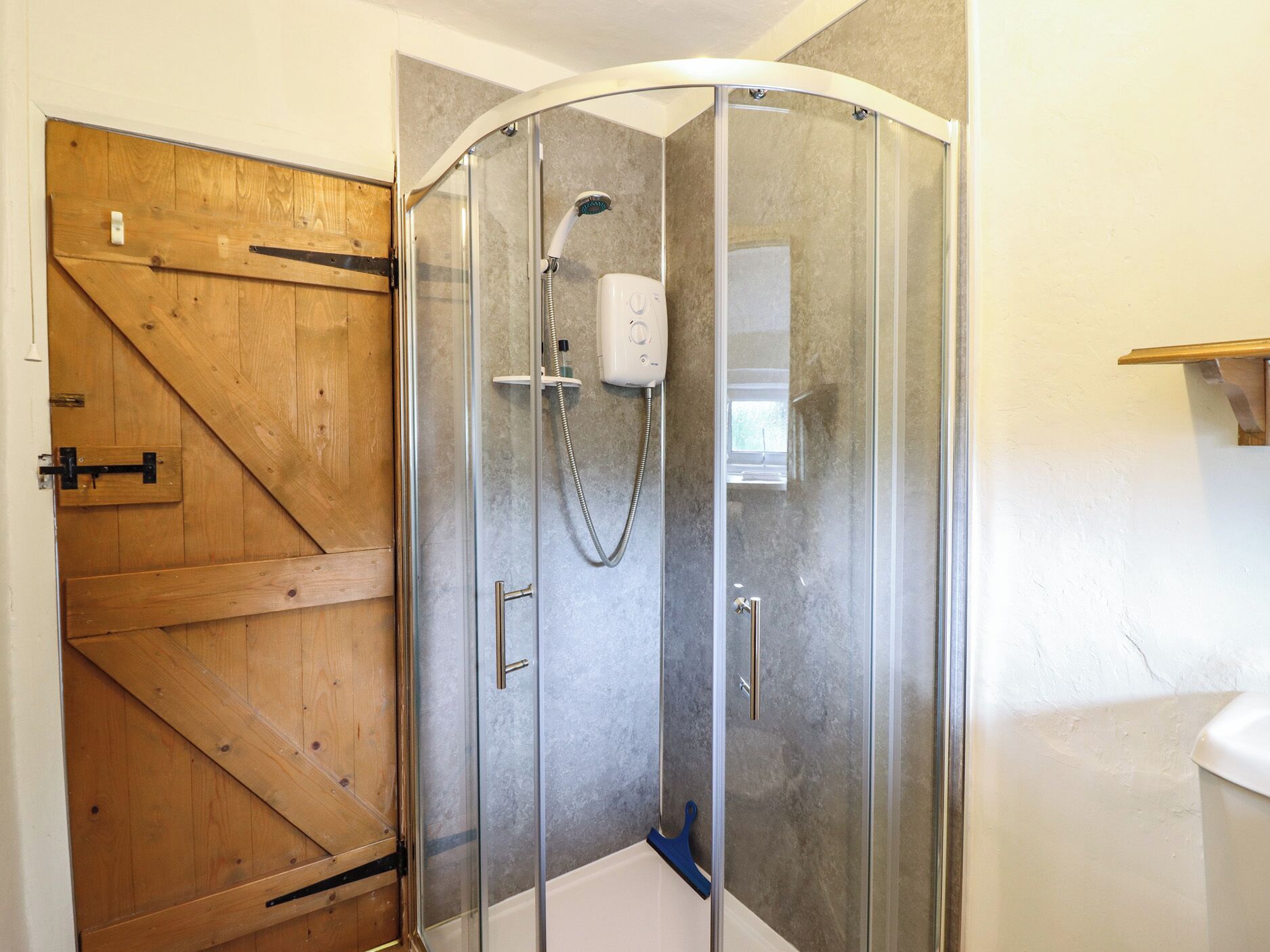 Eine Duschkabine mit Glastür, eine Holztür links und eine weiße Wand.