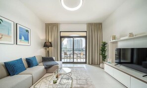 A modern living room with a sofa, coffee table, TV, and balcony with curtains.