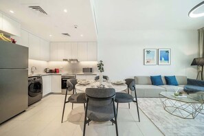 A modern kitchen with built-in appliances, a dining area with a round table and chairs, and a living area with a sofa and a coffee table.