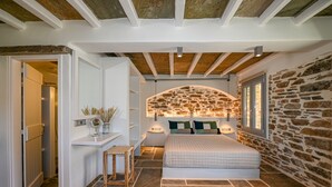A bedroom with a stone wall, a bed, a bedside table, and a window. - Villa 'Celini House 2' with Mountain View, Wi-Fi and Air Conditioning (Tinos)