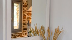 A bathroom vanity with a mirror, a small vase with dried plants, and a window with a view of a stone wall. - Villa 'Celini House 2' with Mountain View, Wi-Fi and Air Conditioning (Tinos)