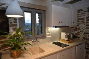 A kitchen with a stone wall, a window with a view, a sink, cabinets, and a hanging light fixture.