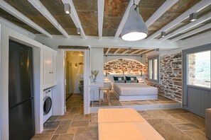 A compact bedroom with a stone wall, a bed, a washing machine, and a ceiling with exposed beams.