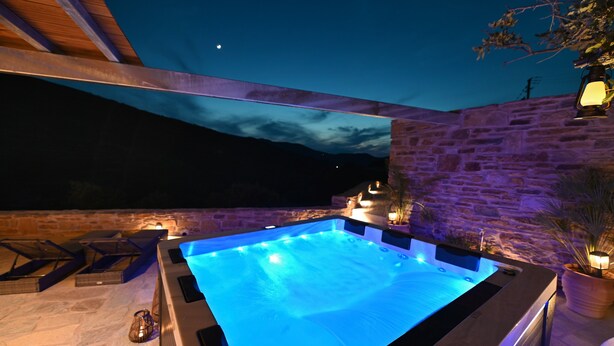 A hot tub with a stone wall backdrop, under a wooden structure, with a night sky view. - Villa 'Celini House 2' with Mountain View, Wi-Fi and Air Conditioning (Tinos)