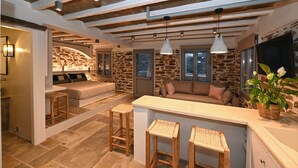 A modern kitchen with a stone wall, wooden beams, and a bar area with stools. - Villa 'Celini House 2' with Mountain View, Wi-Fi and Air Conditioning (Tinos)
