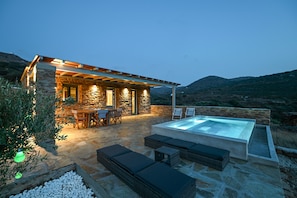 A stone house with a pool, outdoor seating, and a view of the hills.