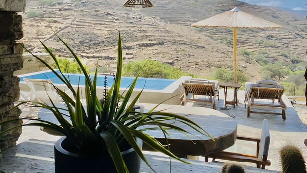 Un área de piscina con sillones reclinables, una lámpara colgante y vistas a un paisaje montañoso.