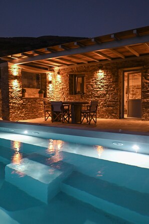 A stone building with a pool, outdoor seating, and a pergola.