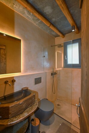 A bathroom with a wooden vanity, a shower, and a window.