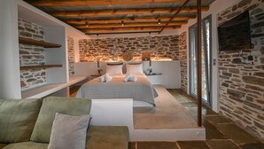 Un dormitorio con paredes de piedra, techo de madera, cama con toallas, mesita de noche y ventana.