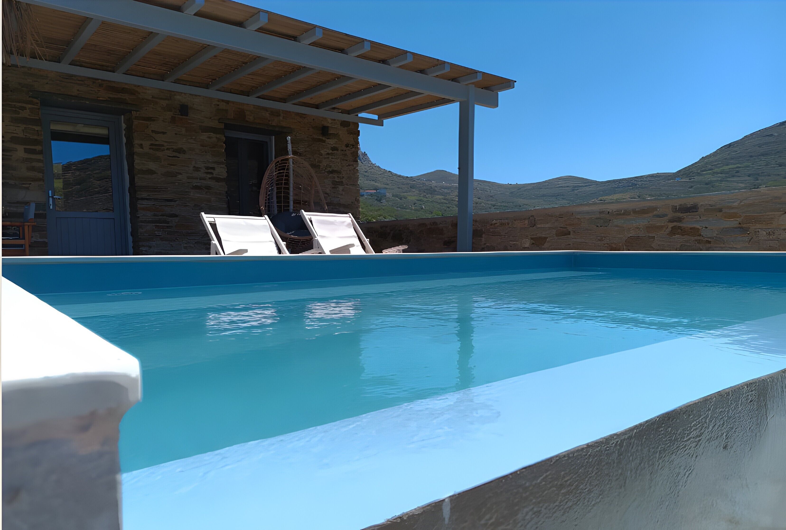 A pool with lounge chairs, a stone building, and a clear view of the mountains.