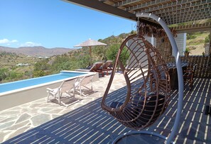 A poolside area with lounge chairs, a wicker chair, and a view of the landscape.