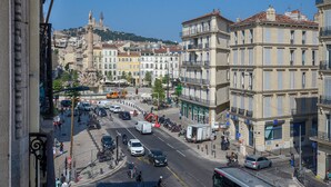 A busy urban street with buildings, a fountain, and a statue in the background.