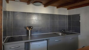 A modern kitchen with grey tiles, stainless steel appliances, and wooden ceiling beams.