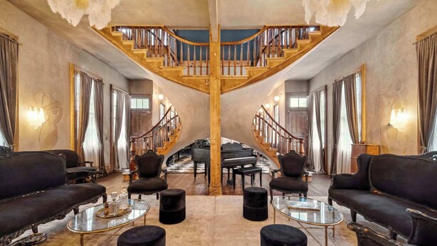 Una lussuosa hall con un'imponente scalinata, eleganti divani neri e un pianoforte a coda.
