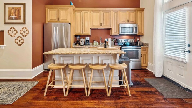 A kitchen with wooden cabinets, a stainless steel refrigerator, a microwave, and a large island with bar stools. - Charming Condo w Patio off Magazine St 2br|1ba (New Orleans)