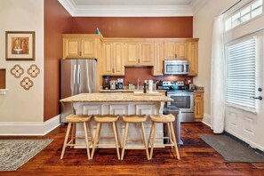 Une cuisine dotée de meubles en bois, d’un réfrigérateur en acier inoxydable, d’un four à micro-ondes et d’un grand îlot central avec des tabourets de bar.