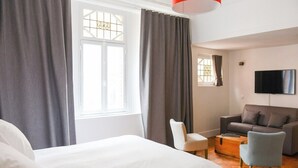 A hotel room with a bed, a grey sofa, a white armchair, a wooden coffee table, and a TV on the wall. - Lille Avenue, Conviviality, Comfort (Lille)