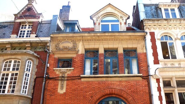 A row of buildings with distinct architectural styles, including a red brick facade with a blue door and balcony. - Lille Avenue, Conviviality, Comfort (Lille)