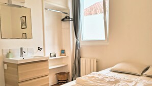 Een slaapkamer met een bed, nachtkastje, spiegel, radiator en raam met gordijnen.