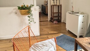 Een moderne woonkamer met een houten vloer, een witte bank, een metalen stoel, een klein tafeltje en een plant in een gele pot.