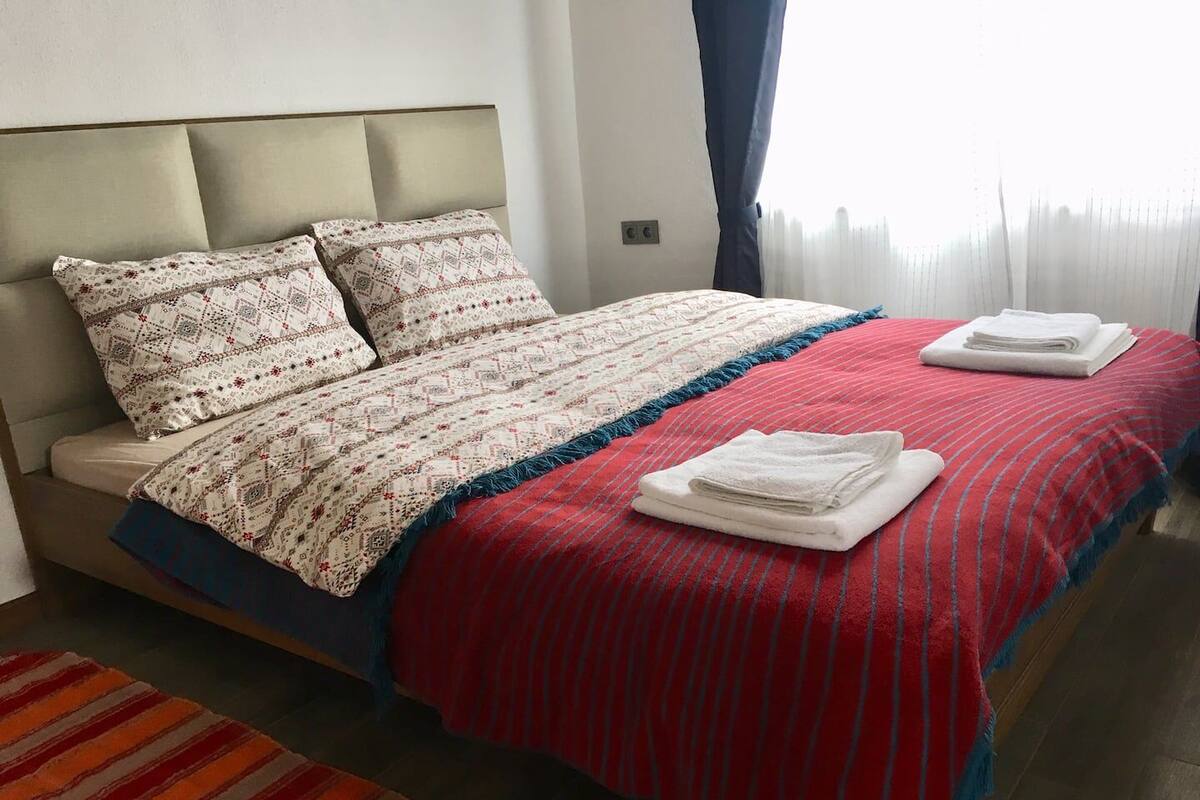 Un letto rifatto con cuscini decorati, una coperta a righe blu e rosse e due asciugamani bianchi piegati.