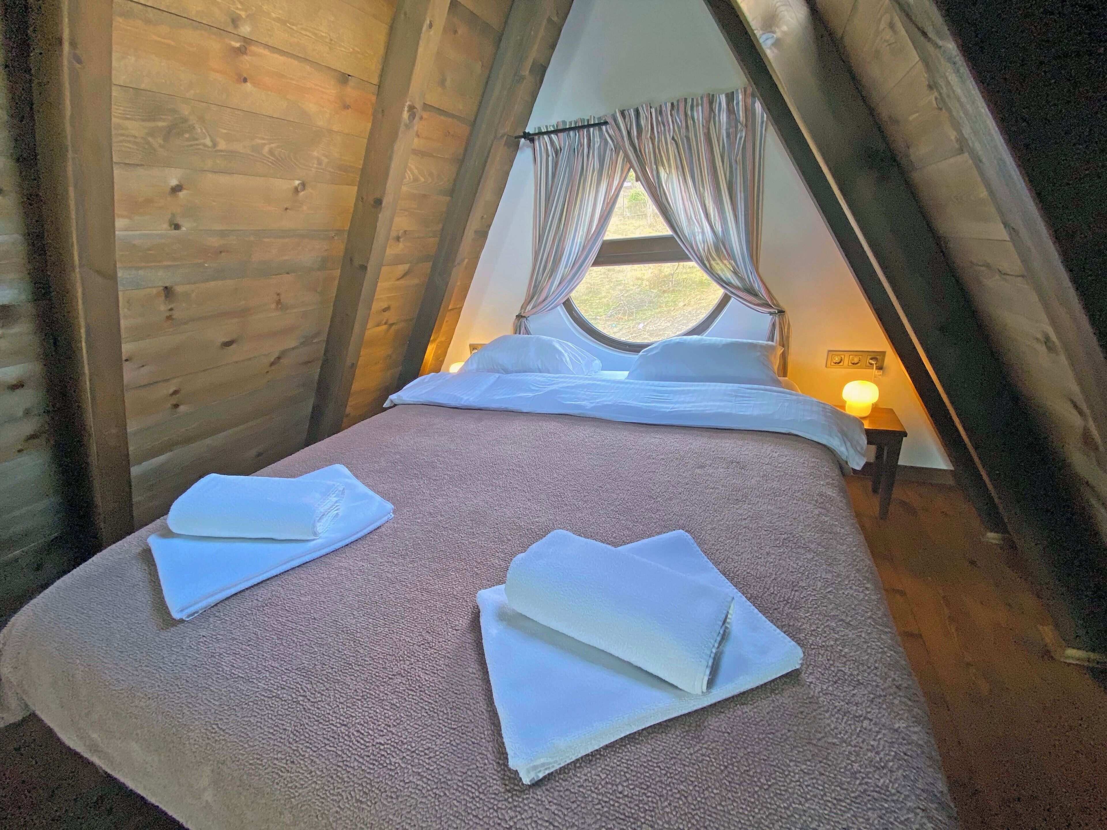 A cozy, triangular-roofed room with a bed, pillows, and a bedside lamp.