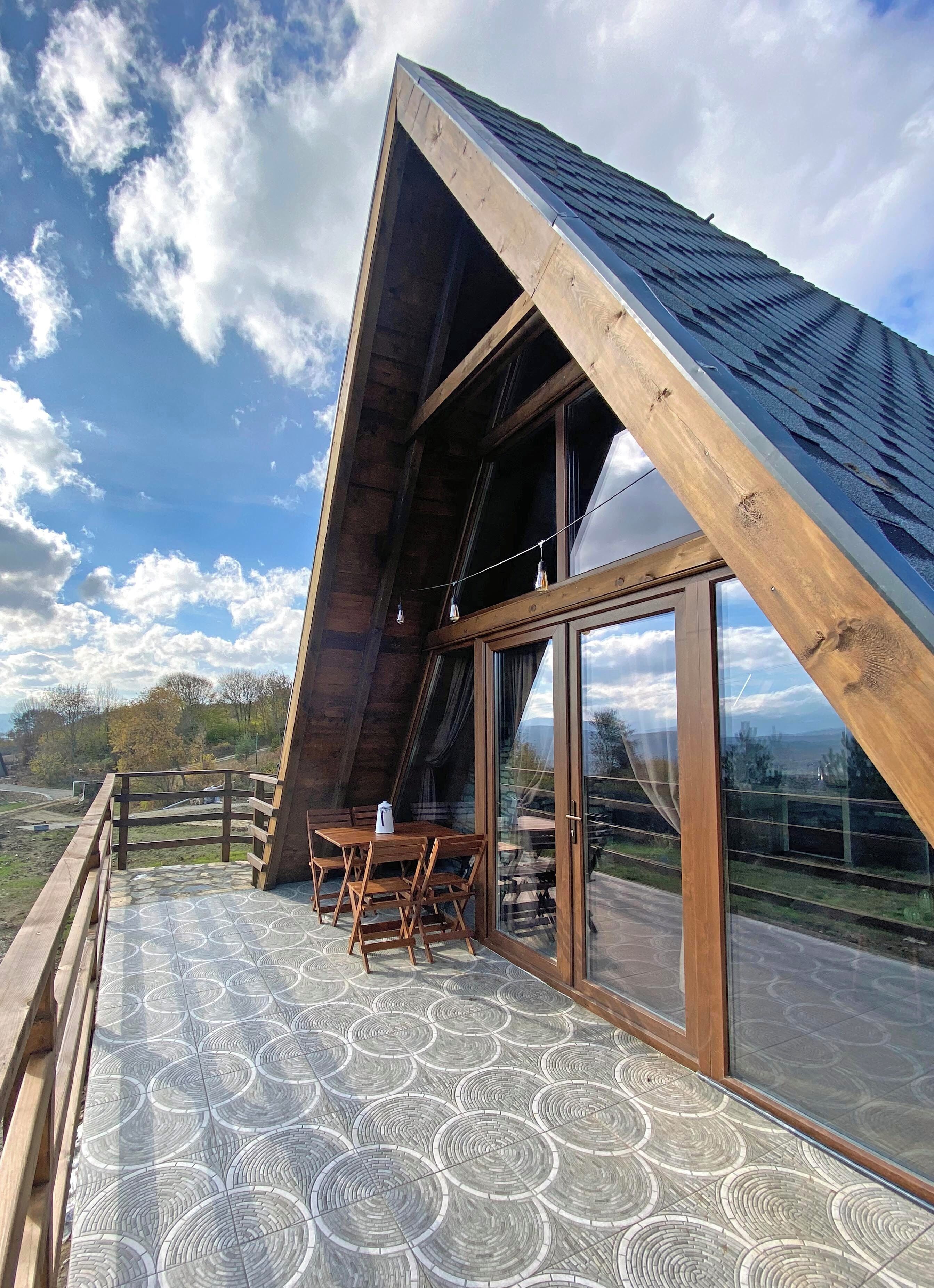 A modern building with a sloped roof, large windows, and a wooden deck with a patterned floor.